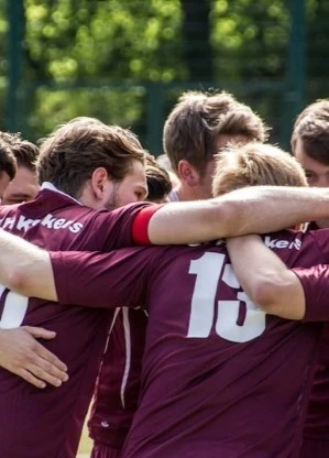 Soccer players in maroon jerseys huddling together in on-field celebration.