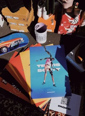 Tabletop with promotional items, Travis Scott poster, car models, and merchandise.
