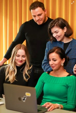 Four people smiling around laptop in warm, well-lit office space.